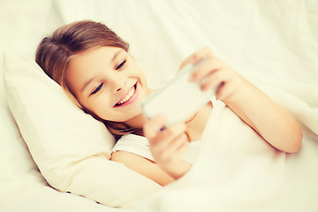 Image showing little girl with smartphone playing in bed