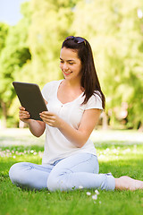 Image showing smiling young girl with tablet pc sitting on grass