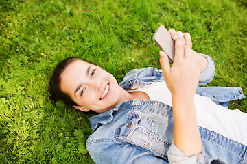Image showing smiling young girl with smartphone lying on grass