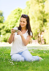 Image showing smiling young girl with smartphone sitting in park