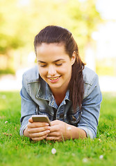 Image showing smiling young girl with smartphone lying on grass