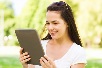 Image showing smiling young girl with tablet pc sitting on grass