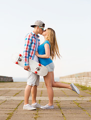 Image showing smiling couple with skateboard kissing outdoors