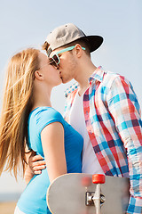 Image showing smiling couple with skateboard kissing outdoors