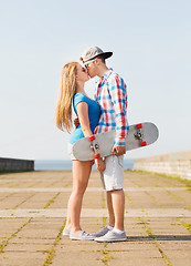 Image showing smiling couple with skateboard kissing outdoors