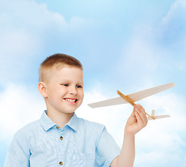 Image showing smiling little boy holding a wooden airplane model