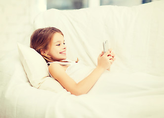 Image showing little girl with smartphone playing in bed