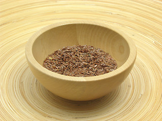 Image showing Wooden bowl with flaxseed on bamboo plate