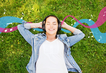 Image showing smiling young girl in headphones lying on grass