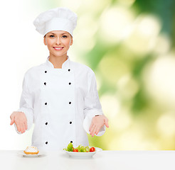 Image showing smiling female chef with salad and cake on plates