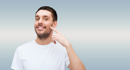 Image showing smiling young handsome man pointing to cheek