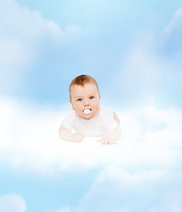 Image showing smiling baby lying on cloud with dummy in mouth