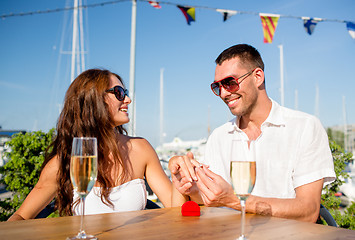 Image showing smiling couple with champagne and gift at cafe