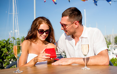 Image showing smiling couple with champagne and gift at cafe