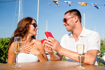 Image showing smiling couple with champagne and gift at cafe