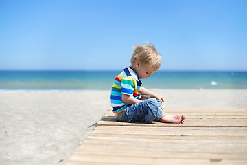 Image showing Boy sitting on a wooden walkway on the beach