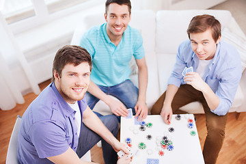 Image showing three smiling male friends playing cards at home