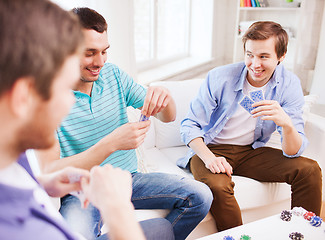 Image showing three smiling male friends playing cards at home