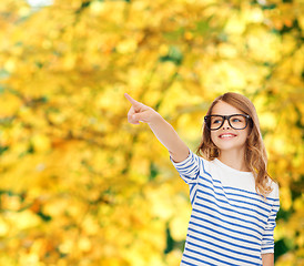Image showing cute little girl in eyeglasses pointing in the air