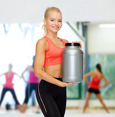 Image showing smiling sporty woman with jar of protein