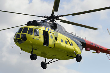 Image showing The yellow MI-8 helicopter flies against clouds with an open doo