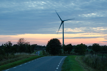 Image showing Wind turbine by a winding road at late evening