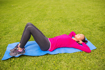 Image showing smiling woman doing exercises on mat outdoors