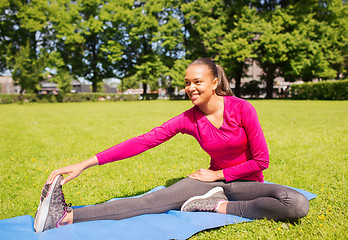 Image showing smiling woman stretching leg on mat outdoors