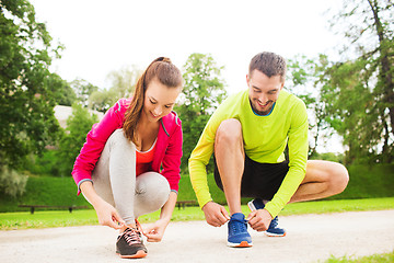 Image showing smiling couple tying shoelaces outdoors