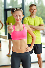 Image showing smiling man and woman showing thumbs up in gym