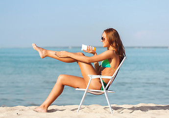 Image showing smiling young woman sunbathing in lounge on beach