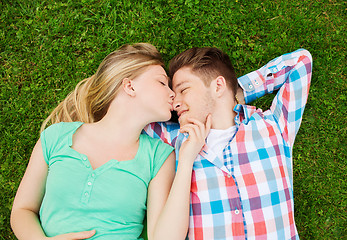 Image showing smiling couple lying on grass and kissing in park