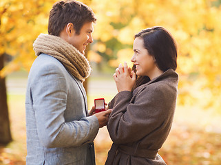 Image showing smiling couple with red gift box in autumn park