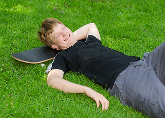 Image showing Laughing guy relax on skateboard in park grass