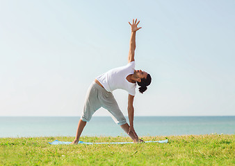 Image showing smiling man making yoga exercises outdoors