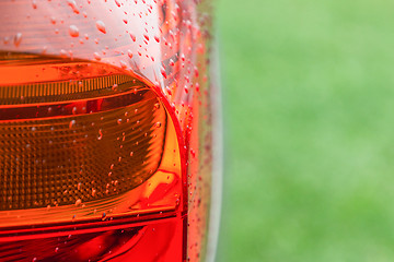 Image showing Wet tail lights of modern car against green grass