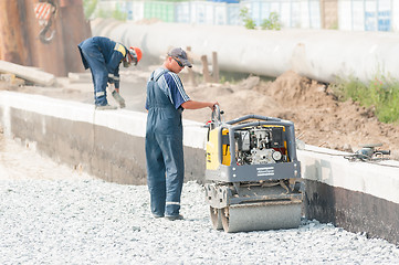 Image showing Worker stamps filling brick by road roller