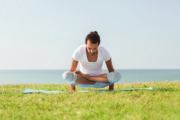 Image showing smiling man making yoga exercises outdoors