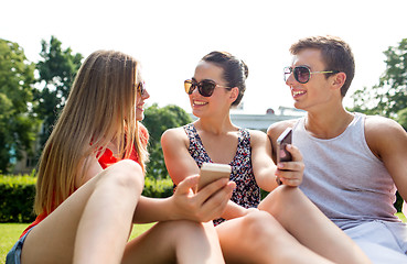 Image showing smiling friends with smartphones sitting on grass