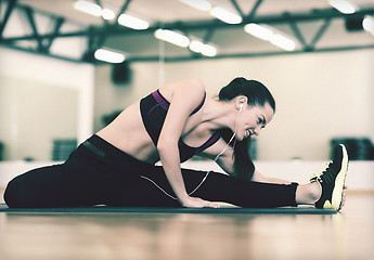 Image showing smiling woman stretching on mat in the gym