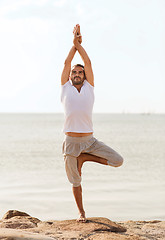 Image showing smiling man making yoga exercises outdoors