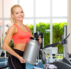 Image showing smiling sporty woman with jar of protein