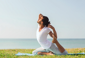 Image showing smiling man making yoga exercises outdoors