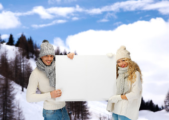 Image showing smiling couple in winter clothes with blank board
