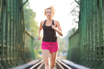 Image showing Active female athlete running on railaway tracks.