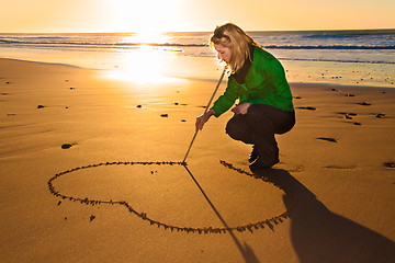 Image showing Woman drowing a heart shape in the sand.