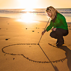 Image showing Woman drowing a heart shape in the sand.