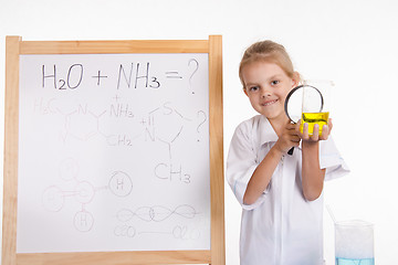 Image showing Girl chemist examines liquid in flask under a magnifying glass