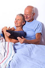 Image showing Senior Couple with Tablet and Newspaper in Bed