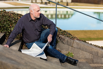 Image showing Man sitting on steps reading a newspaper